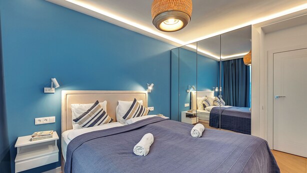 Ein modernes Hotelzimmer mit einem großen Bett, einem Nachttisch, einem Spiegel und einem Kleiderschrank.