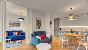Ein modernes Wohnzimmer mit einem blauen Sofa, einem grauen Sofa, einem runden Holzesstisch und weißen Stühlen.