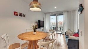 Ein modernes Wohnzimmer mit einem Holzesstisch, weißen Stühlen, einem grauen Sofa und einem Fernseher.