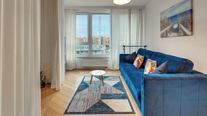 Ein modernes Wohnzimmer mit einem blauen Sofa, einem runden Couchtisch und Blick auf die Stadt durch große Fenster.