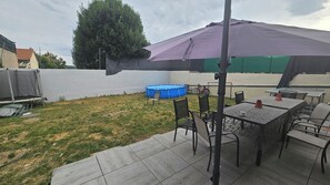 Un jardin avec un trampoline, une piscine bleue et un espace patio aménagé avec des tables et des chaises.