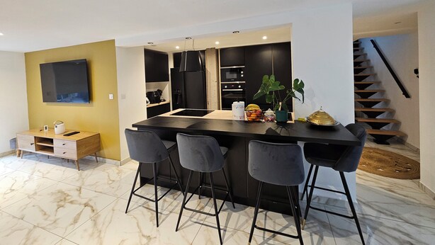 Een moderne keuken met een centraal eiland, barstoelen en een trap naar een hoger niveau.