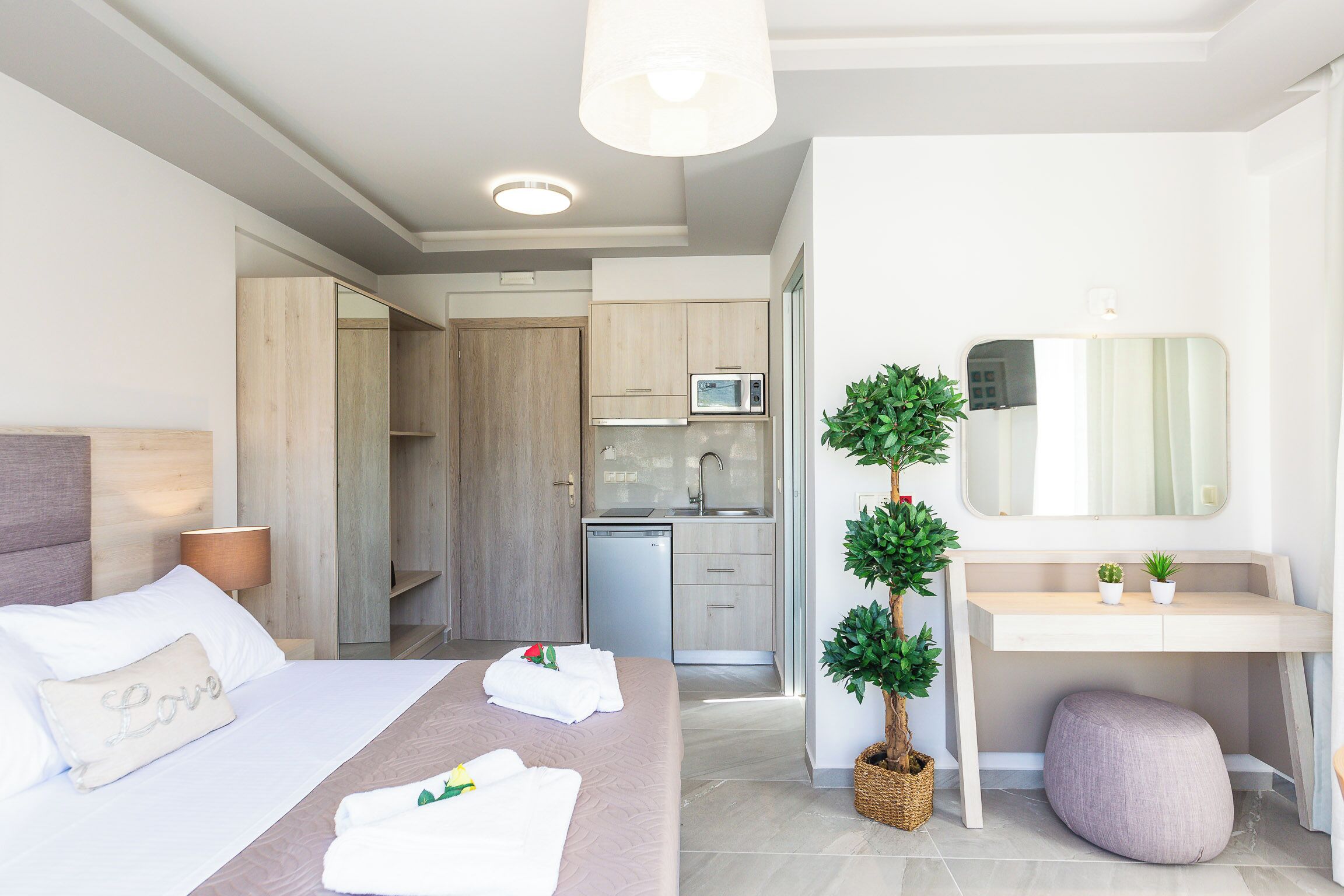 Habitación de hotel moderna con cama, mesita de noche, un pequeño escritorio, un espejo y vista al área de la cocina.