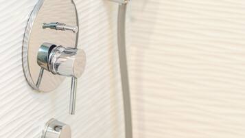 A bathroom with a wall-mounted shower system, including a handheld showerhead and a fixed showerhead.