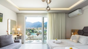 A hotel room with a balcony, a bed, a sofa, and a desk with a lamp. - Akrogiali Apartments (Mylopotamos)