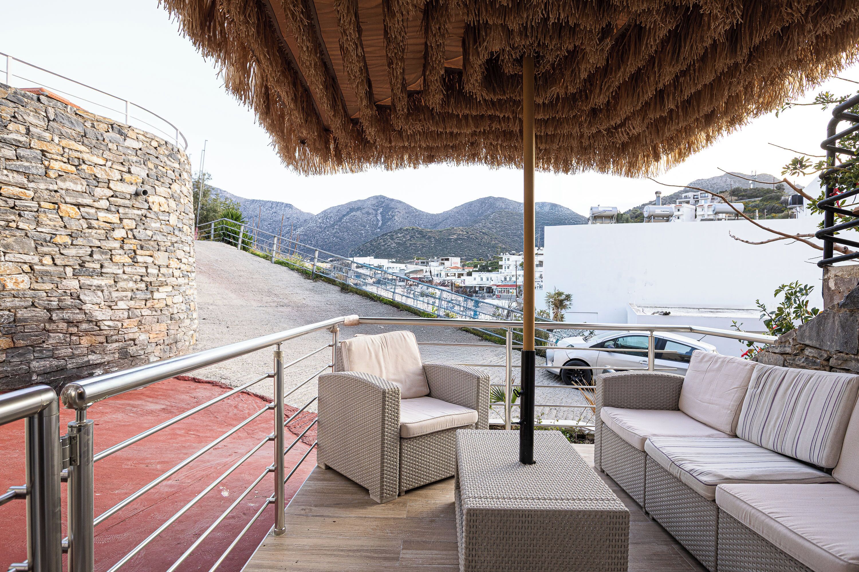 A balcony with wicker furniture, a stone wall, and a view of the sea and mountains.