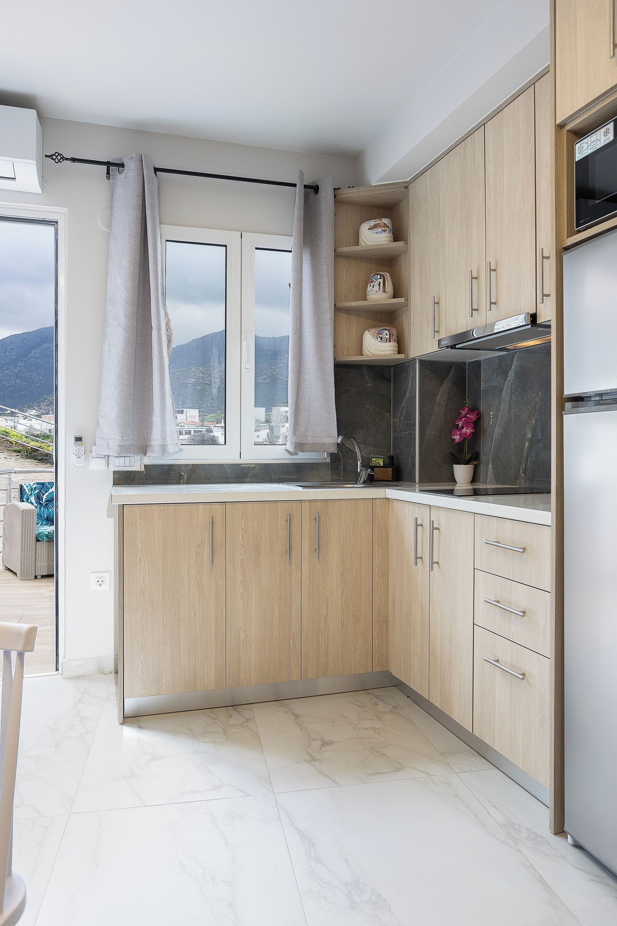 A modern kitchen with wooden cabinets, a marble countertop, and a view of the mountains.