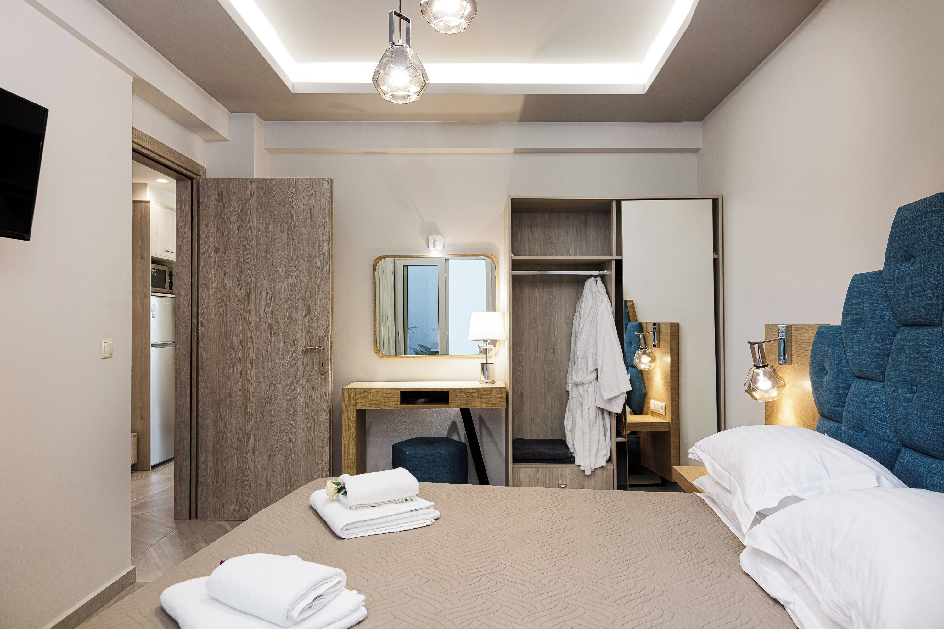 Een moderne hotelkamer met een groot bed, een bureau met spiegel, een kledingkast en een badkamer zichtbaar door een geopende deur.