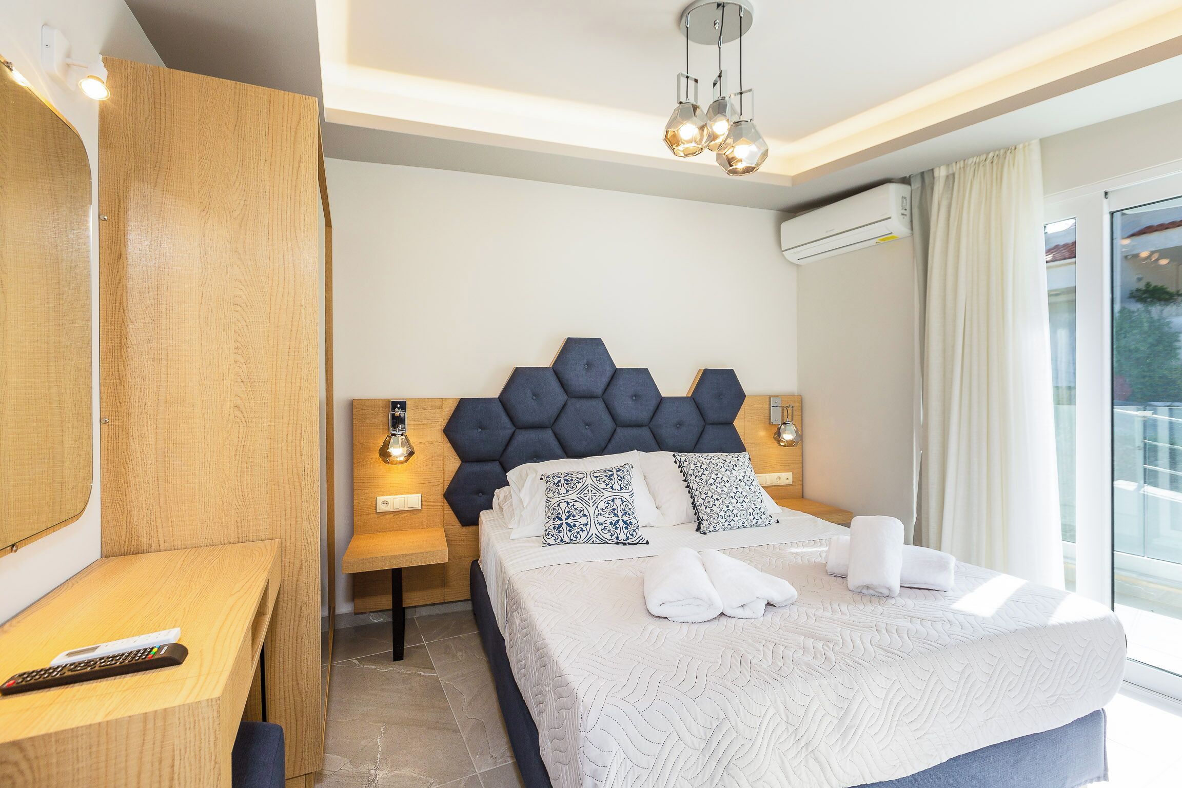 A modern hotel room with a large bed, a wooden desk, and a view of the outdoors.