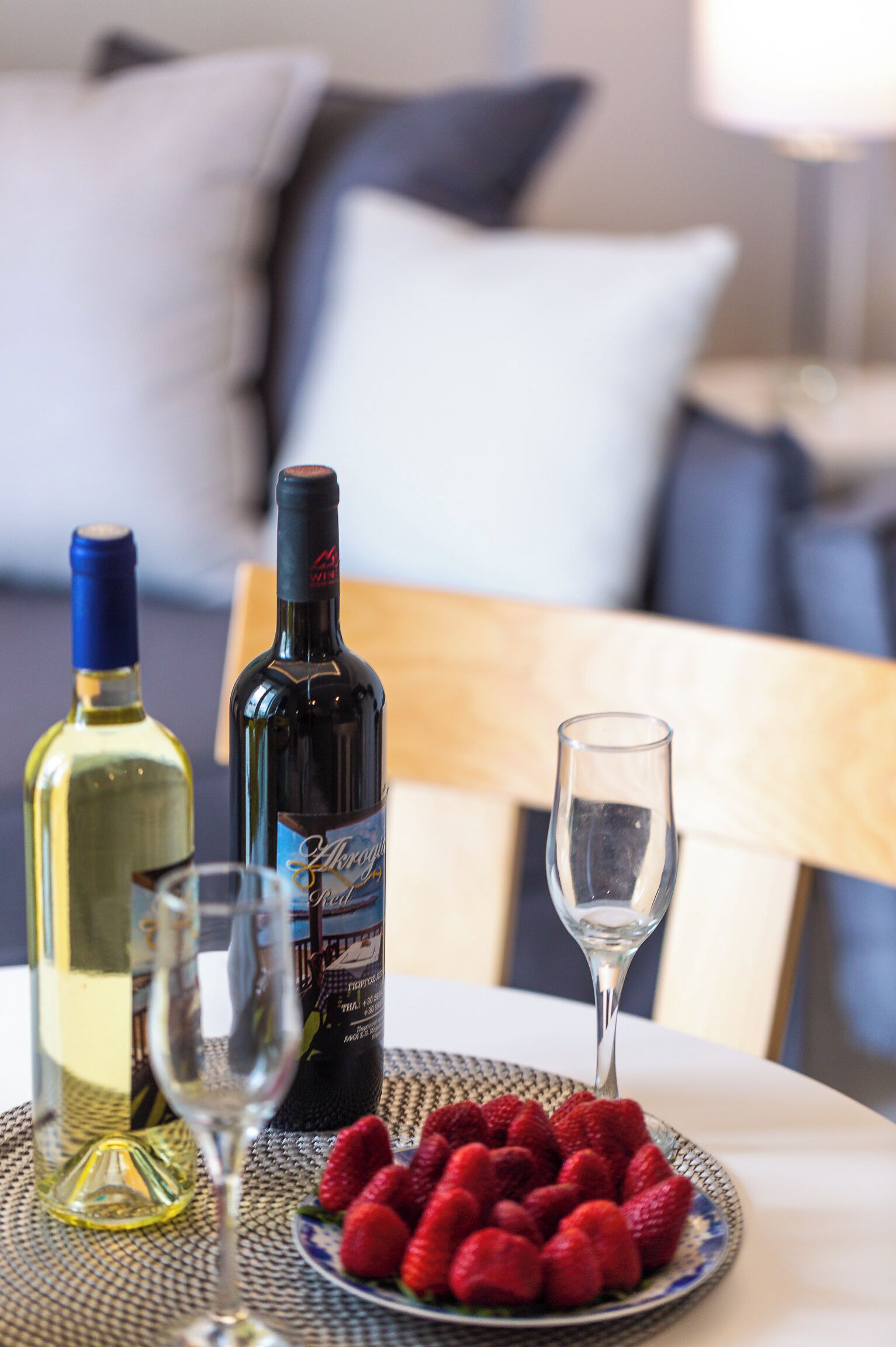 Una mesa con dos botellas de vino, una copa y un plato de fresas.
