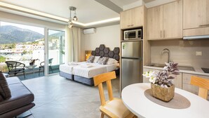 A modern hotel room with a balcony, a bed, a dining area, and a kitchenette. - Akrogiali Apartments (Mylopotamos)