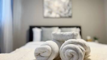 A neatly made bed with rolled white towels and a plain wall with a single piece of abstract art.
