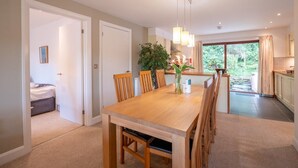 A modern dining area with a wooden table and chairs, a potted plant, and a view of the garden through the glass door. - Pet friendly Croft Cottage (Truro)