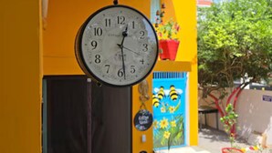 A yellow building with a large clock hanging from the ceiling, a door, and a checkered floor. - The Nomad Cave (Lucknow)