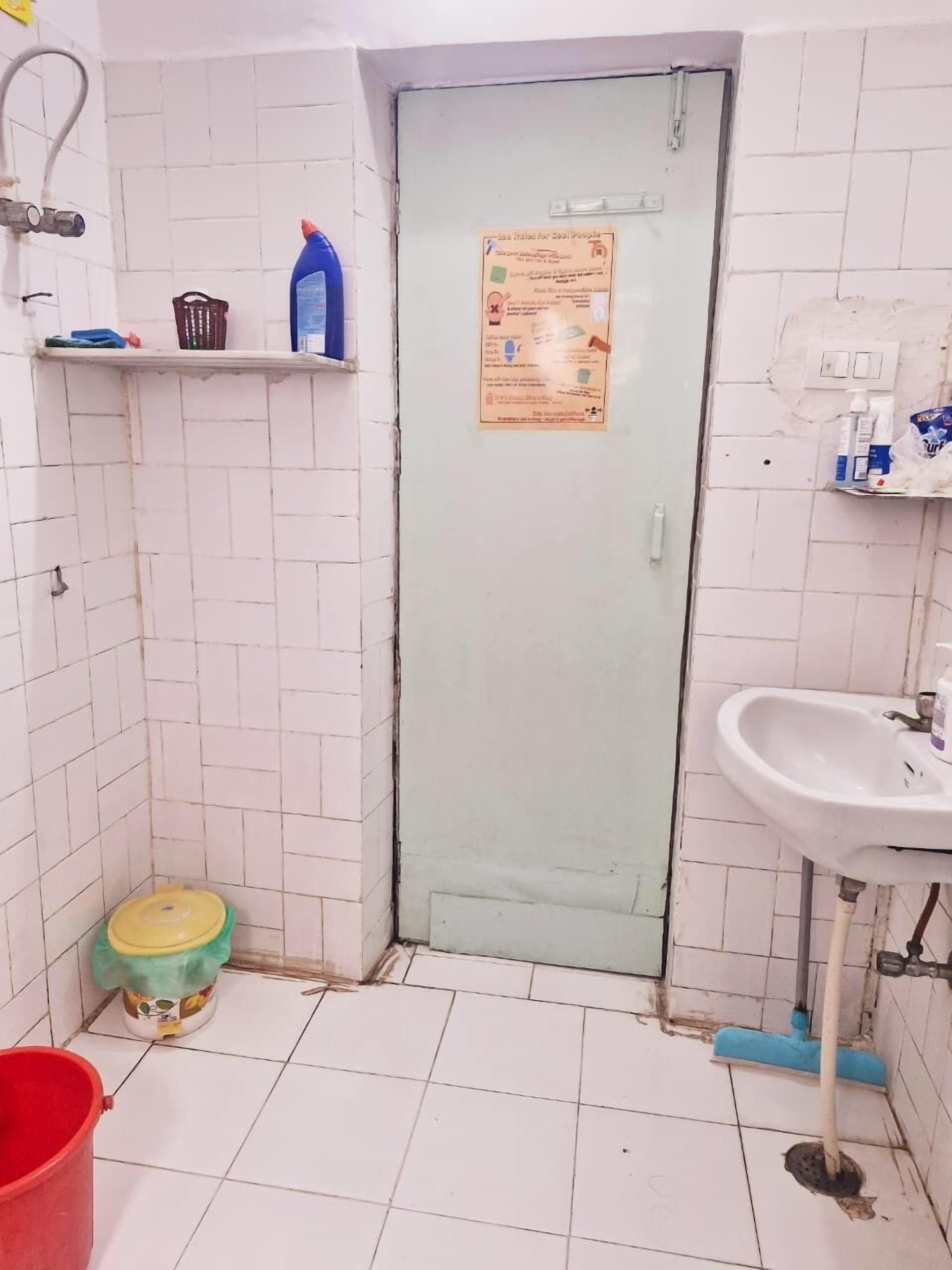 A small, tiled bathroom with a white sink, a door with a notice, and a red bucket.