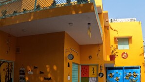 A brightly colored building with a yellow facade, a blue gate with bee designs, and a motorcycle parked in front. - The Nomad Cave (Lucknow)