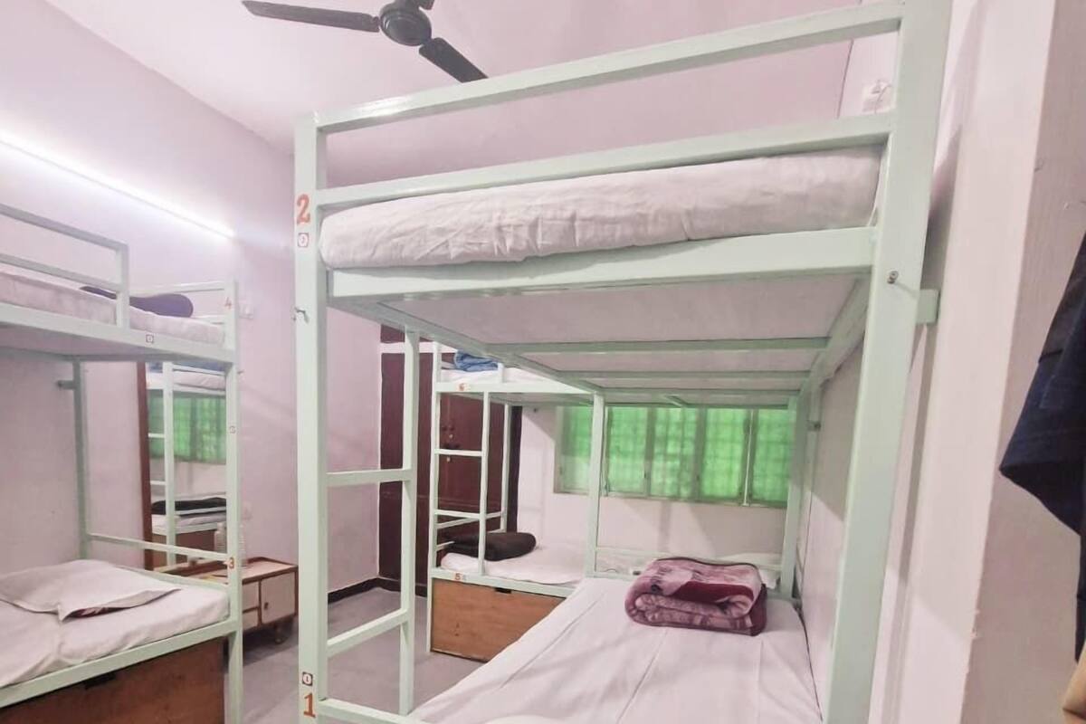 Ein Schlafsaalzimmer mit Etagenbetten, einem Deckenventilator und einem Fenster mit grünen Vorhängen.