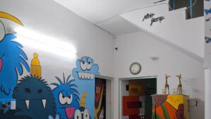 A reception area with a desk labeled "RECEPTION," a computer, and a colorful wall with cartoonish monster decorations. - The Nomad Cave (Lucknow)