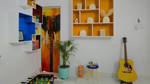 A room with a foosball table, a guitar, a potted plant, and shelves with various items. - The Nomad Cave (Lucknow)