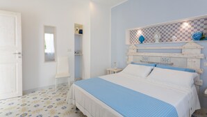 A bedroom with a bed, a chair, a nightstand, and a wall-mounted shelf with decorative items.