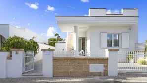A modern two-story house with a white exterior, a gated entrance, and a small balcony on the upper floor.
