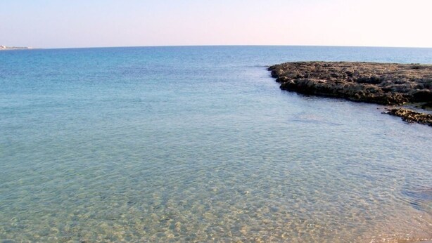 A clear view of a beach with calm waters and a rocky shoreline.