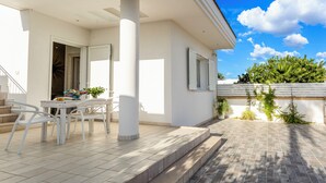 A modern house with a patio area featuring a white table and chairs, a small garden, and a view of the sky and trees.