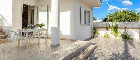 A modern house with a patio area featuring a white table and chairs, a small garden, and a view of the sky and trees.