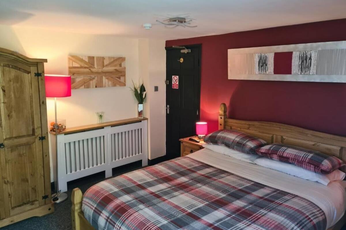 Quarto com colcha xadrez, guarda-roupa de madeira, luminária vermelha e porta com placa de proibido fumar.