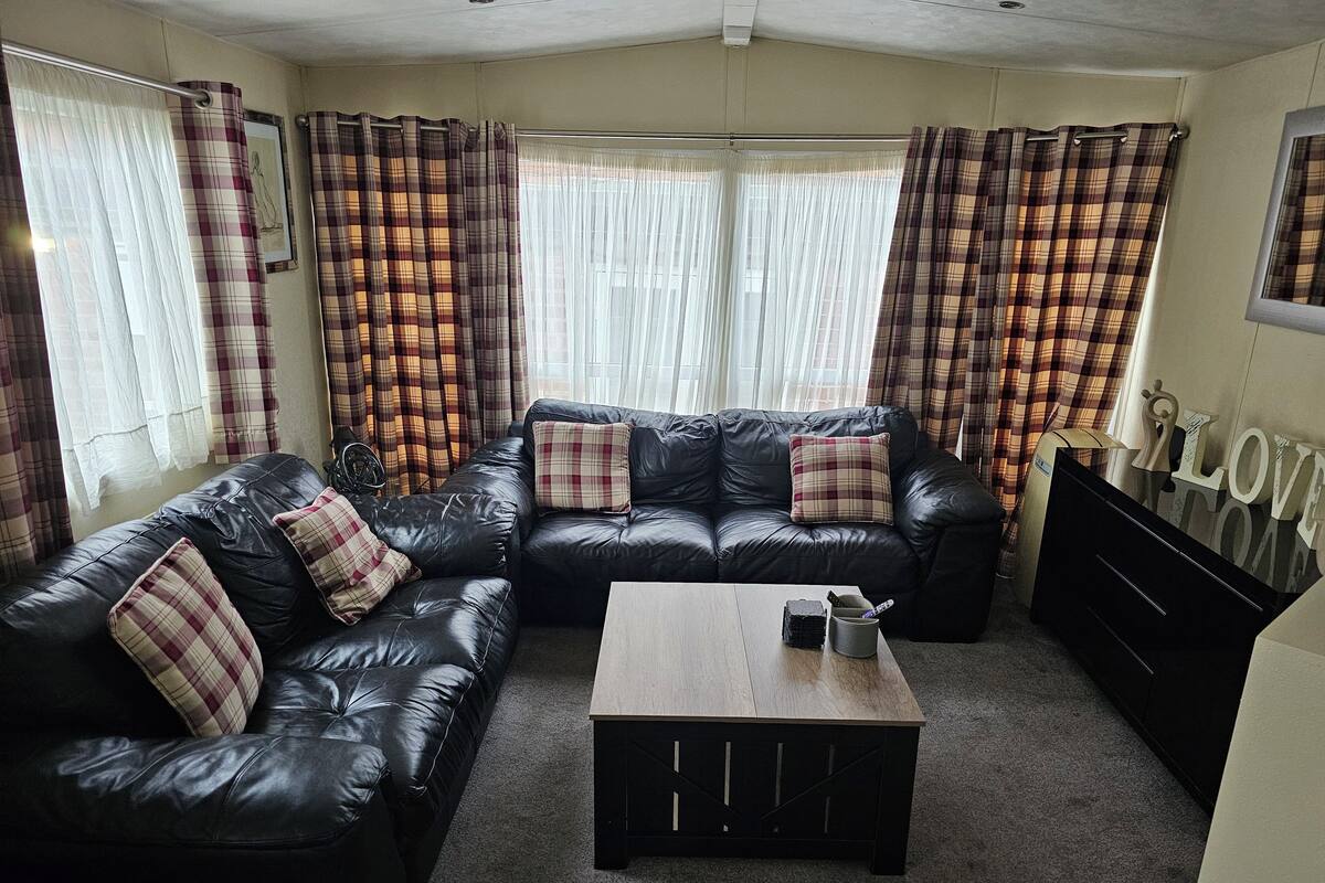 Uma sala de estar com sofá de couro preto, mesa de centro de madeira e cortinas xadrez.