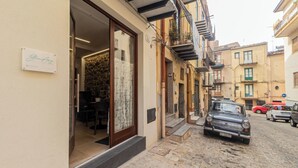 A narrow street with a building entrance, a stone-paved ground, and parked cars.
