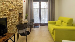 A living room with a stone wall, a yellow sofa, a TV on a wooden table, and a dining area with chairs and a small table.