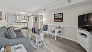 A modern living room with a grey sofa, white wicker chairs, a coffee table, and a flat-screen TV. - 10% off 3-7 nights thru Dec. 2BR 2BA oceanVIEW condo Cherry Grove. Peaceful area (North Myrtle Beach)