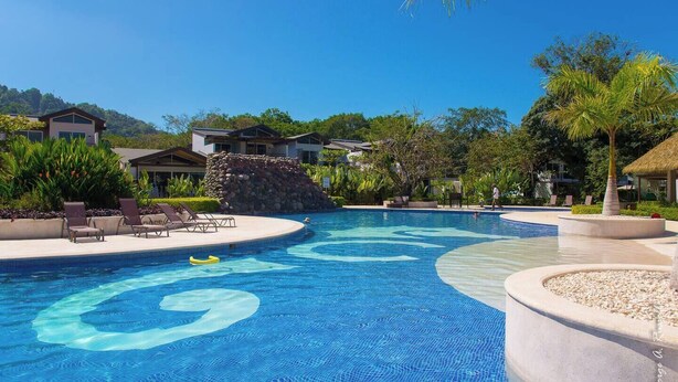 Una piscina con diseño circular, sillas de descanso y una estructura con techo de paja.