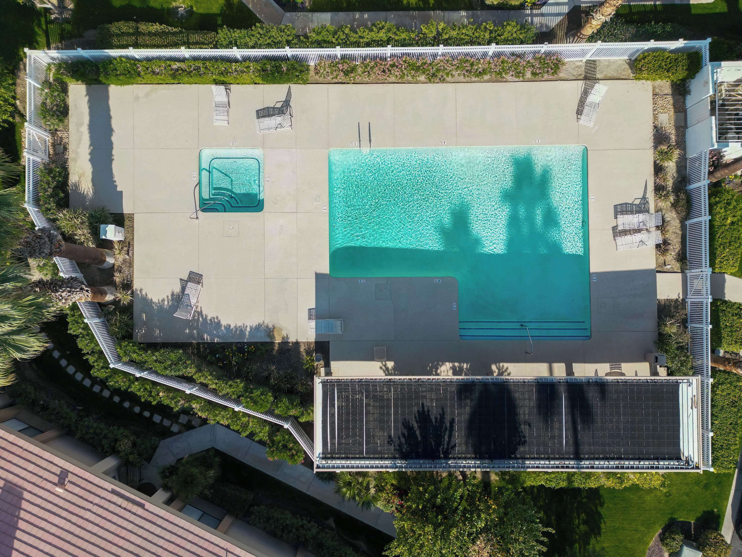 An aerial view of a rooftop pool area with a large pool, lounge chairs, and a small hot tub.