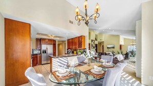 A modern kitchen with wooden cabinets, a central island, and a dining area with a glass table and chairs. - Luxury PGA West  3BR 2BA Condo (La Quinta)