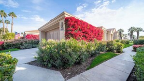 A residential building with a well-maintained garden, a clear sky, and an American flag. - Luxury PGA West  3BR 2BA Condo (La Quinta)
