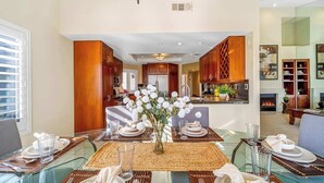 A dining area with a glass table, wooden chairs, and a vase of white flowers. - Luxury PGA West  3BR 2BA Condo (La Quinta)