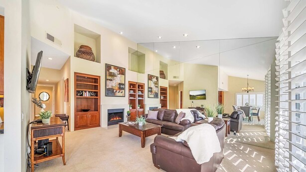 A spacious living room with a fireplace, a sofa, a coffee table, and a TV mounted on the wall. - Luxury PGA West  3BR 2BA Condo (La Quinta)