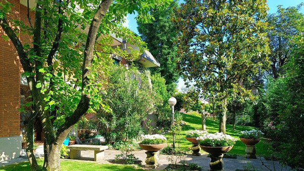 Ein gepflegter Garten mit einem Backsteingebäude, Steinbänken und großen Pflanzgefäßen.