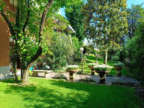 A well-maintained garden with a brick building, stone benches, and large planters. - Garden house, two-bedroom house, garden, private parking space   (Casorezzo)