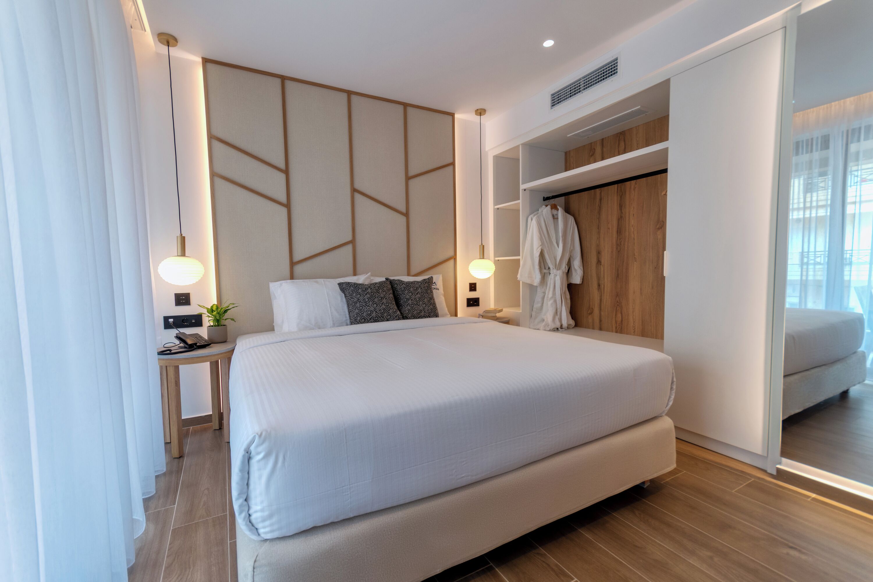 Een moderne hotelkamer met een groot bed, nachtkastjes, een badjas en een kledingkast.