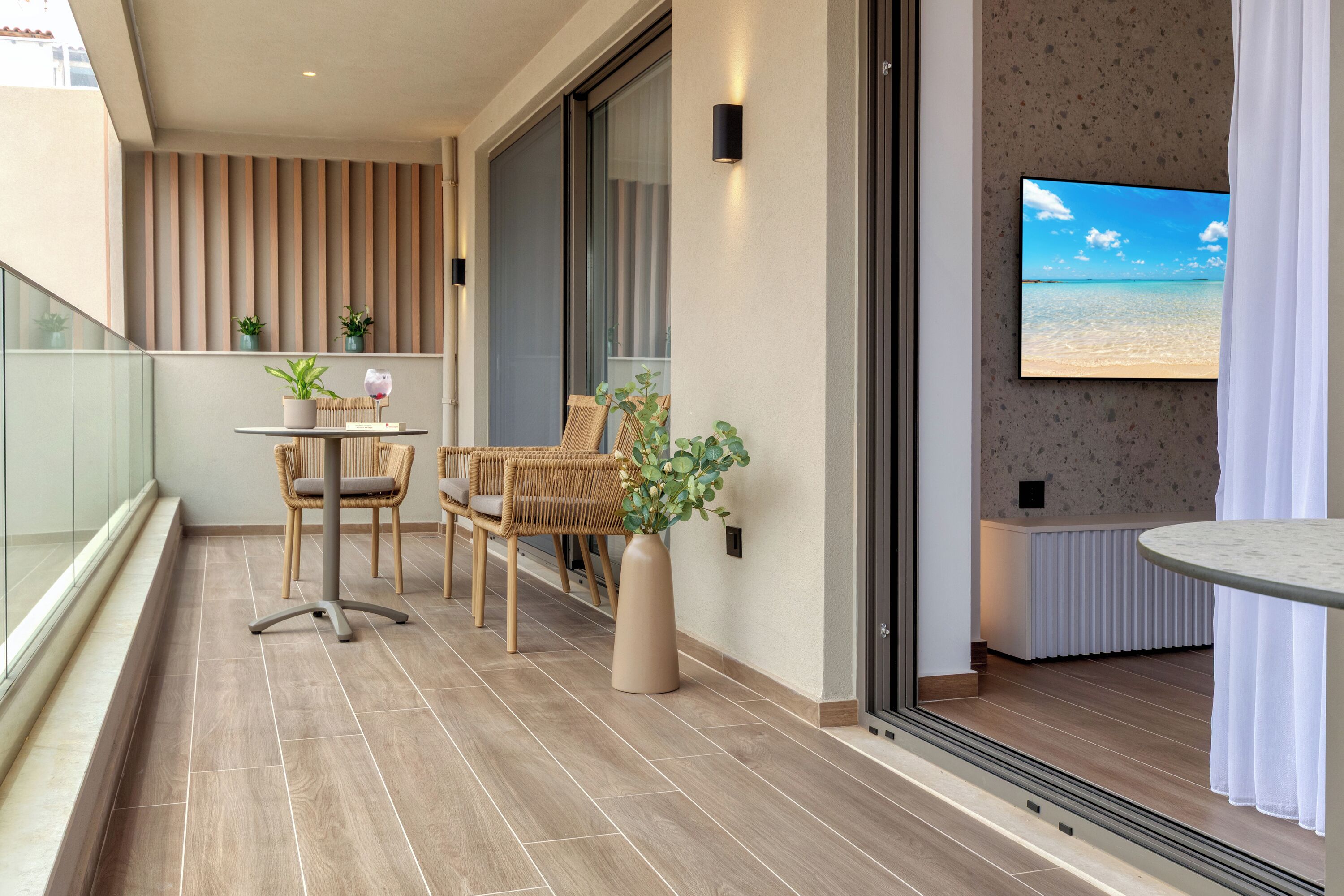 A balcony with a table and chairs, a potted plant, and a TV screen displaying a beach scene.