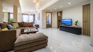 Un salon moderne avec un ensemble de canapés, une table basse, un téléviseur posé sur un meuble noir et une porte en bois.