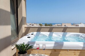 A hot tub with two glasses of water, a potted plant, and a view of the sea.