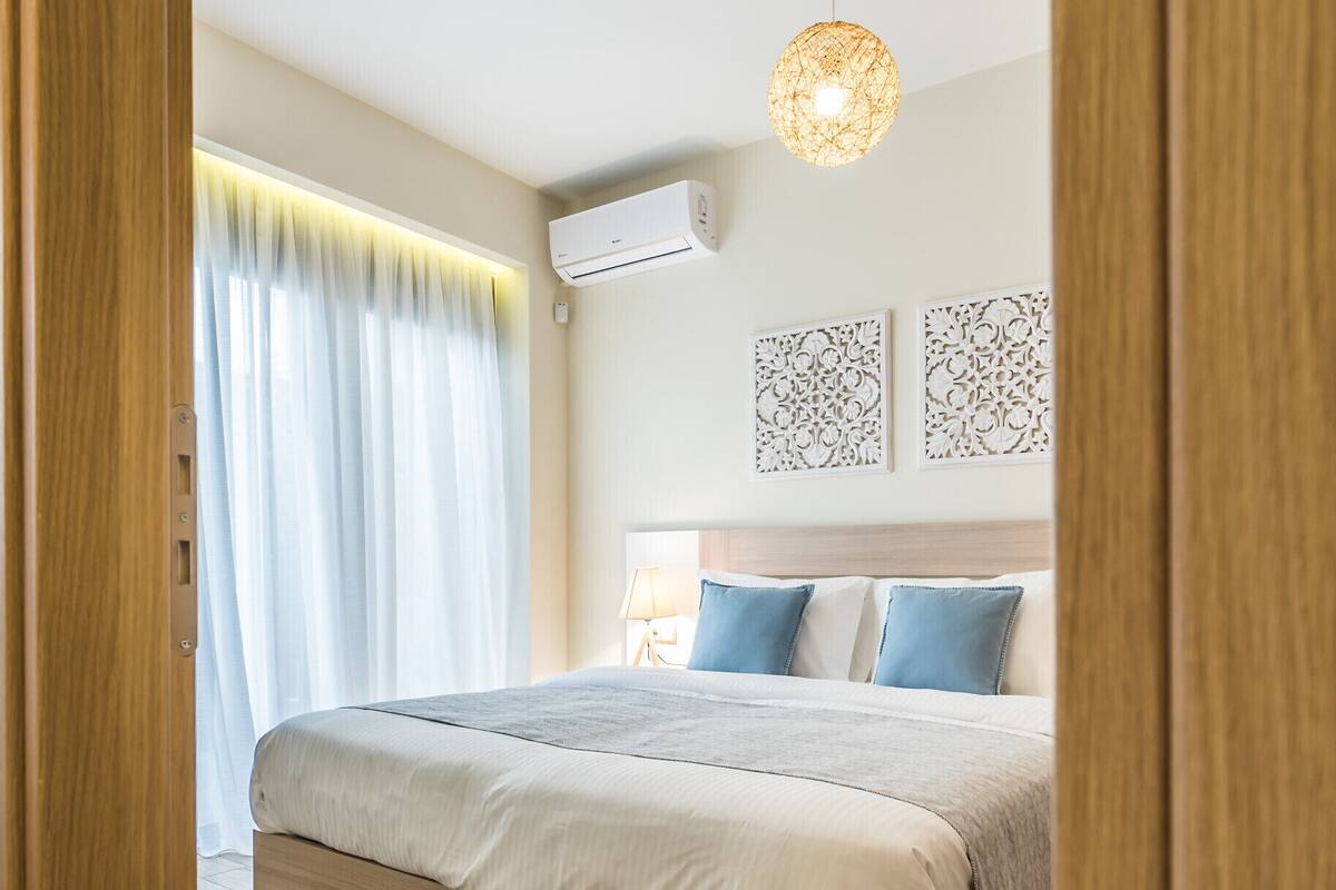 Une chambre avec un lit en bois, un luminaire suspendu et une fenêtre avec des rideaux.
