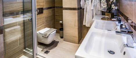 A modern bathroom with a glass shower enclosure, a toilet, a sink with a mirror, and two white robes hanging on a rack.