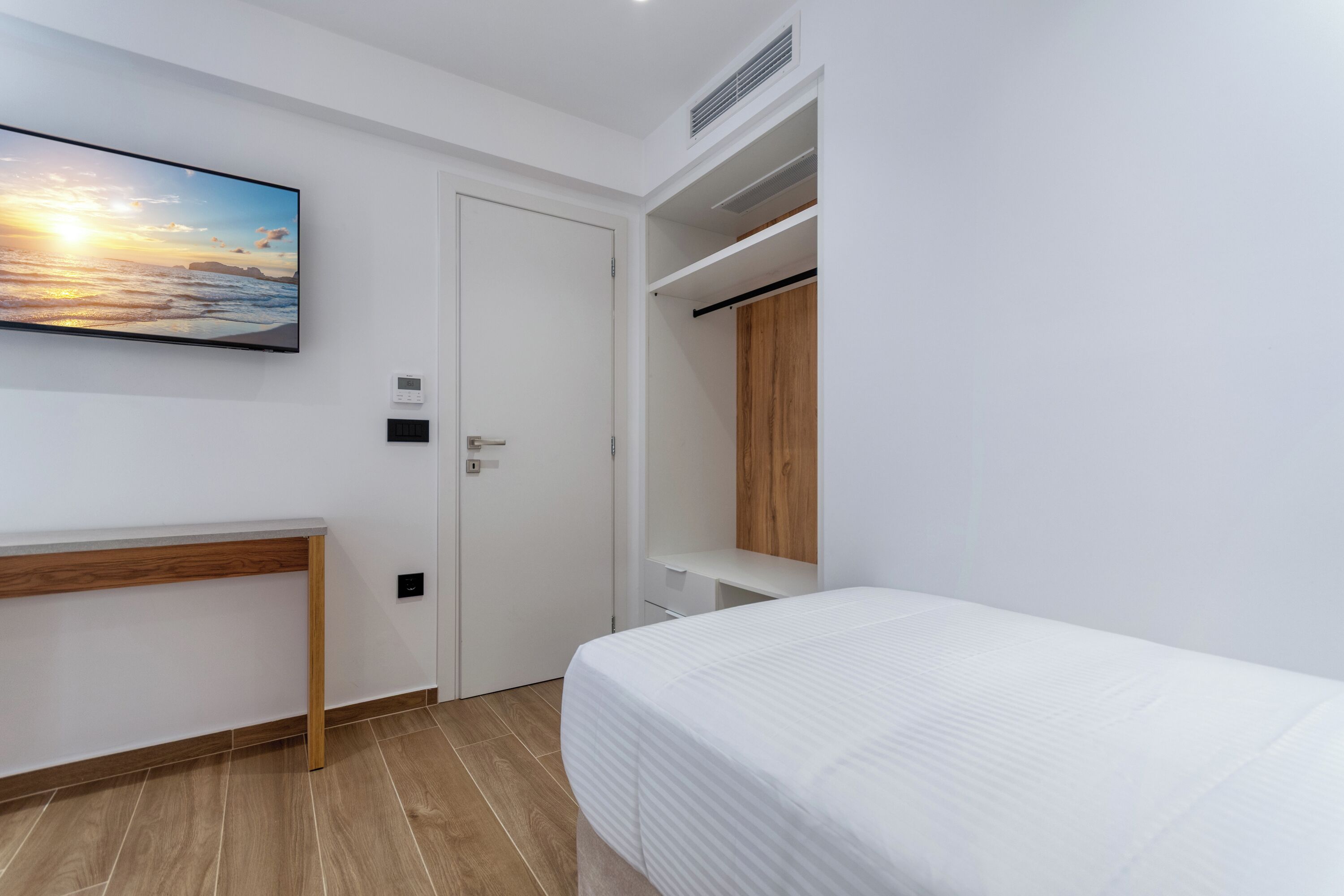 A bedroom with a bed, a desk, a wardrobe, and a painting on the wall.