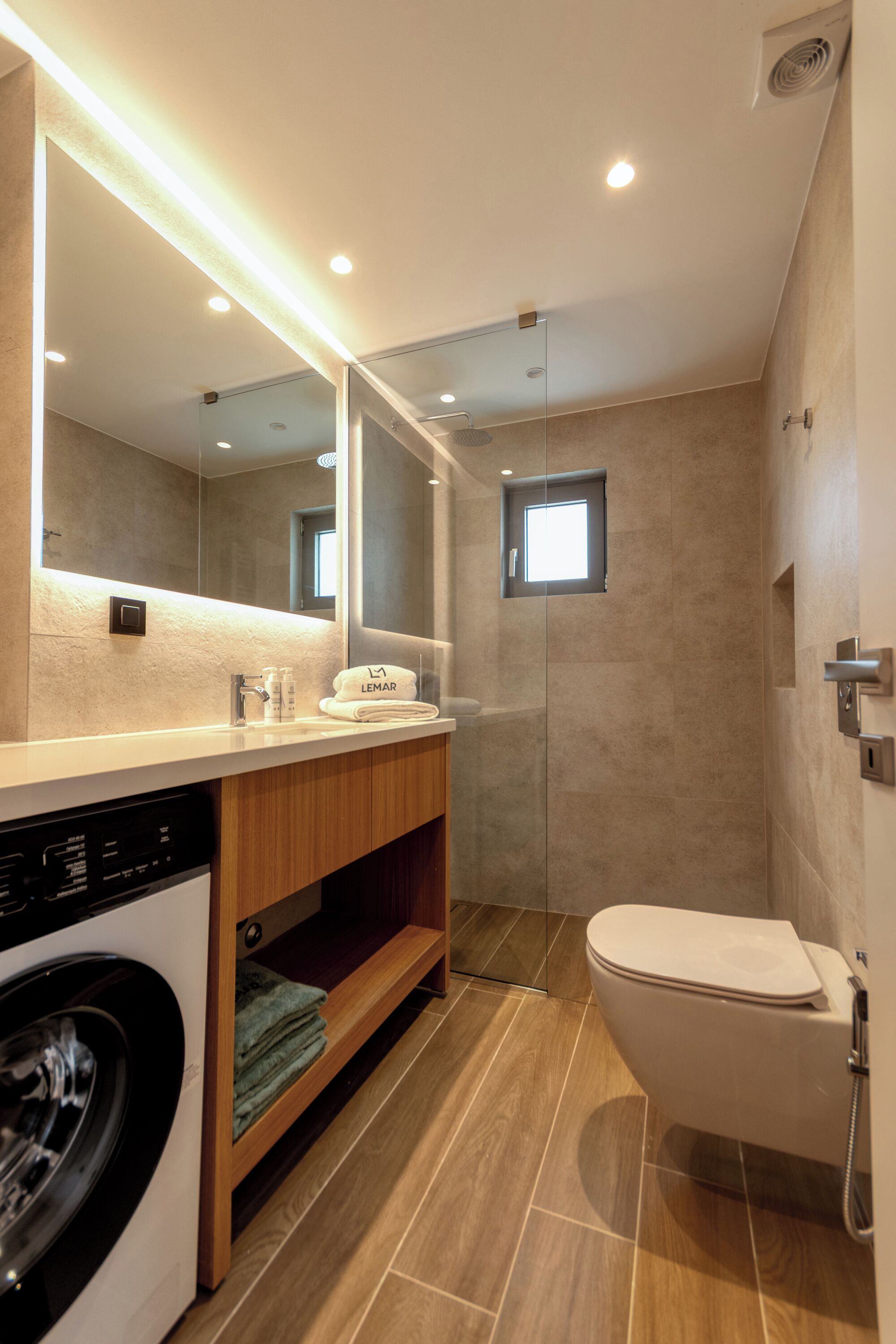 A modern bathroom with a washing machine, a toilet, a glass-enclosed shower, and a large mirror.