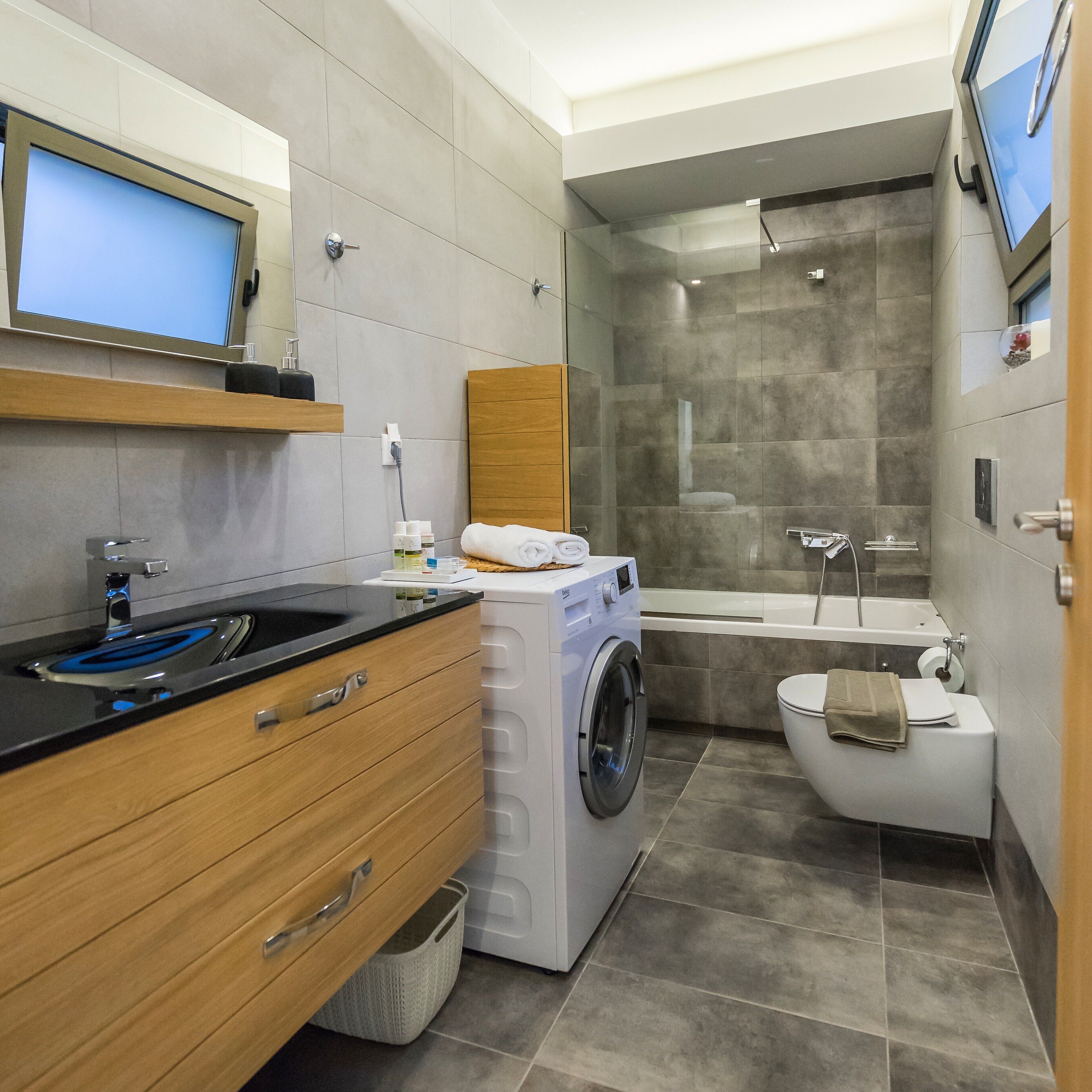 A modern bathroom with a washing machine, toilet, and bathtub.